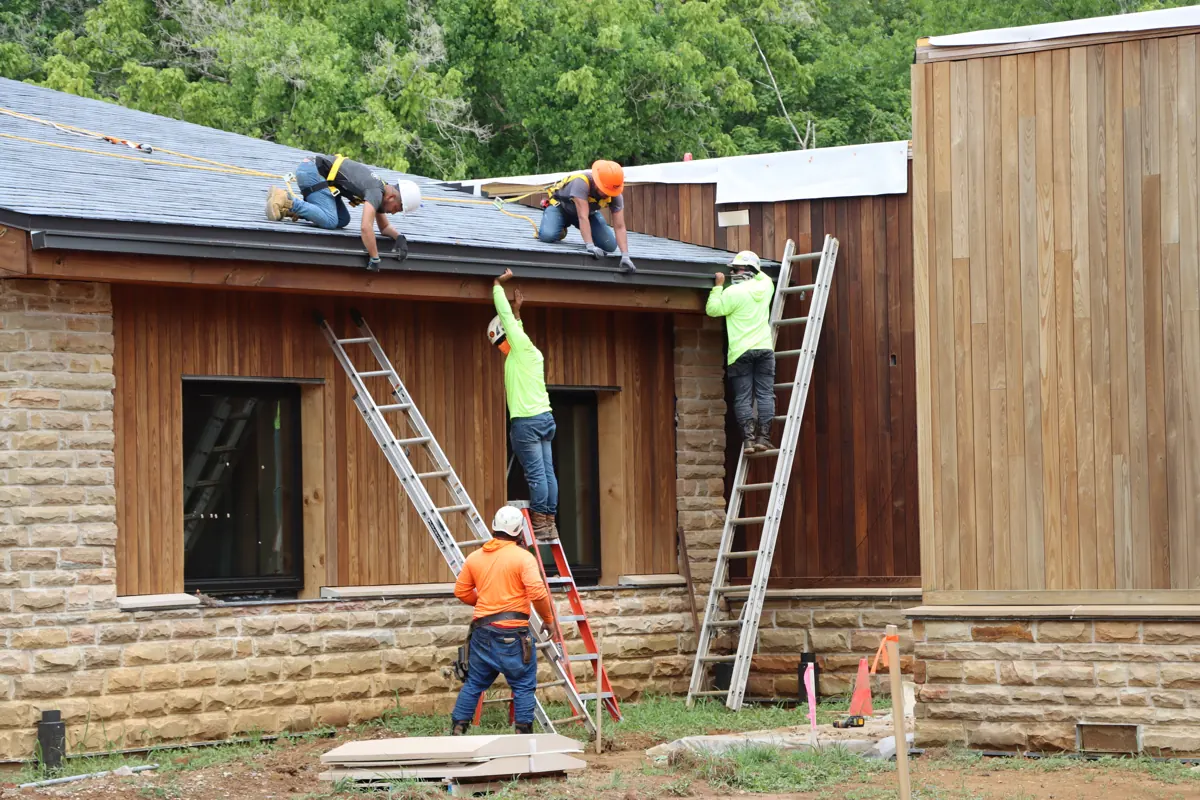 Crew hanging new gutters along the edge of a shingle roof