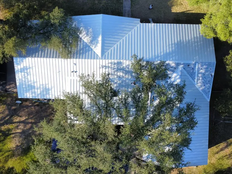 White standing seam metal roof on a ranch home among oak trees
